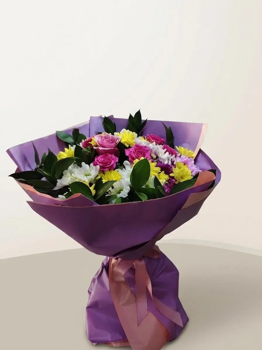 Mor ve pudra ambalaj içinde pembe güller, sarı ve beyaz krizantemler ile koyu yeşil yapraklardan oluşan buket.